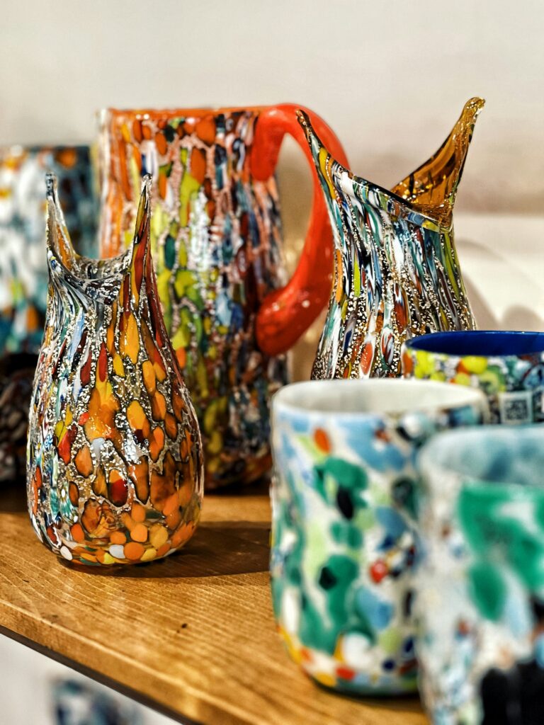 muranoglass Murano glass cups and pitchers sitting on a wooden shelf.